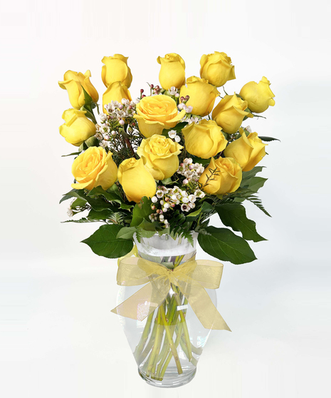 Bright yellow roses with seeded eucalyptus in a clear glass vase. 