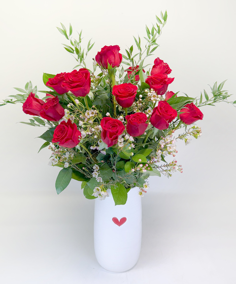 One dozen long stemmed red roses in a vase with river rocks, wax flower and Italian ruscus.