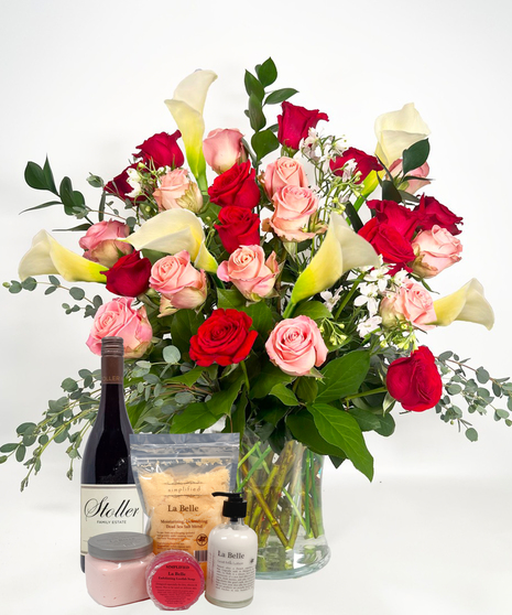 Long stemmed red and pink roeses and white calla lilies in a clear glass vase.