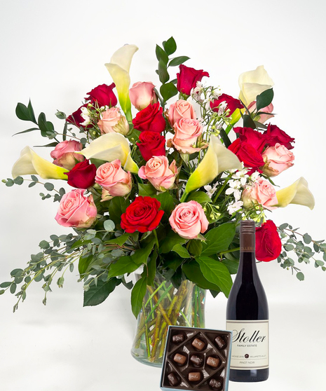 Long stemmed red and pink roeses and white calla lilies in a clear glass vase.