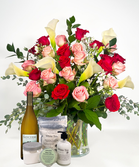 Long stemmed red and pink roeses and white calla lilies in a clear glass vase.