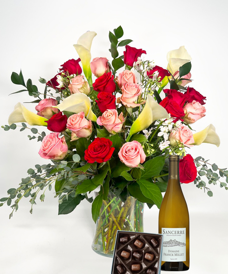 Long stemmed red and pink roeses and white calla lilies in a clear glass vase.