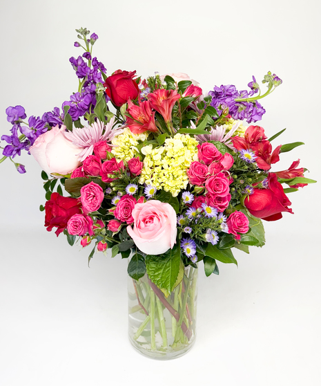 Red cube vase filled with roses in red, pink and lavender with greenery.