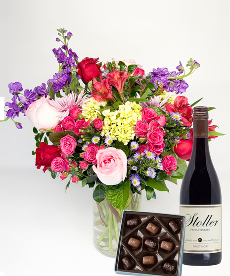 Red cube vase filled with roses in red, pink and lavender with greenery.