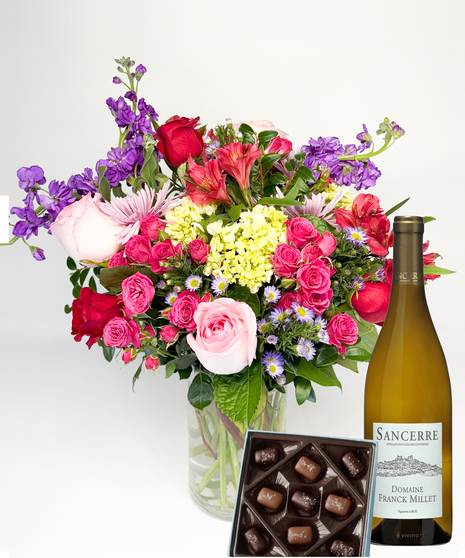 Red cube vase filled with roses in red, pink and lavender with greenery.