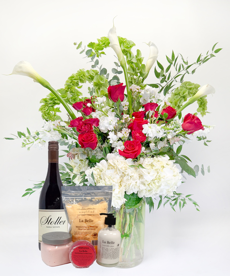 Long stemmed red and pink roeses and white calla lilies in a clear glass vase.