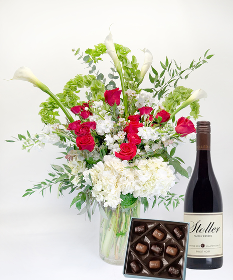 Long stemmed red and pink roeses and white calla lilies in a clear glass vase.