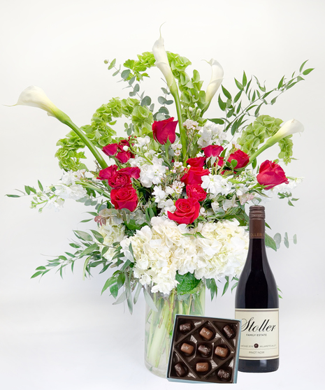 Long stemmed red and pink roeses and white calla lilies in a clear glass vase.