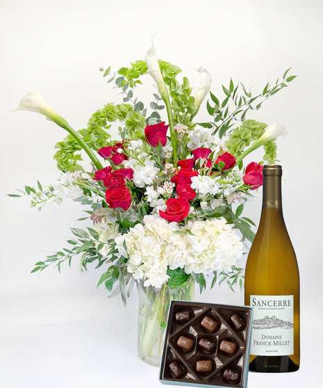 Long stemmed red and pink roeses and white calla lilies in a clear glass vase.