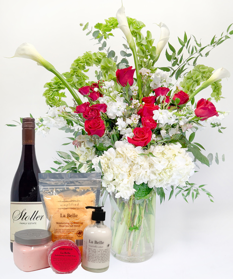 Long stemmed red and pink roeses and white calla lilies in a clear glass vase.