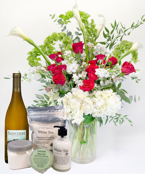 Long stemmed red and pink roeses and white calla lilies in a clear glass vase.