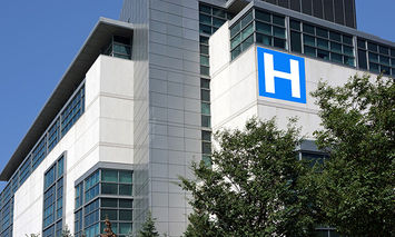 A multistory hospital building displaying a large blue sign with a white 